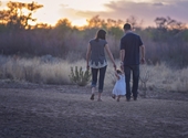Ouders wandelen met hun kindje in de natuur, de opkomende of ondergaande zon tegemoet